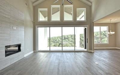 4720 Napoli Shore Dr, Leander, TX 78641 - unfurnished living room with a chandelier, wood finished floors, high vaulted ceiling, a tiled fireplace, and baseboards