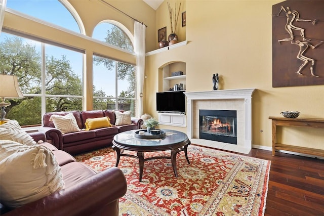 10129 Brimfield Dr, Austin, TX 78726 - living room featuring built in features, hardwood / wood-style flooring, a towering ceiling, baseboards, and a tiled fireplace