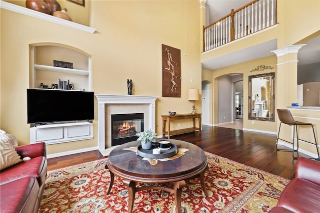 10129 Brimfield Dr, Austin, TX 78726 - living area featuring wood-type flooring, arched walkways, a towering ceiling, a tiled fireplace, and built in features