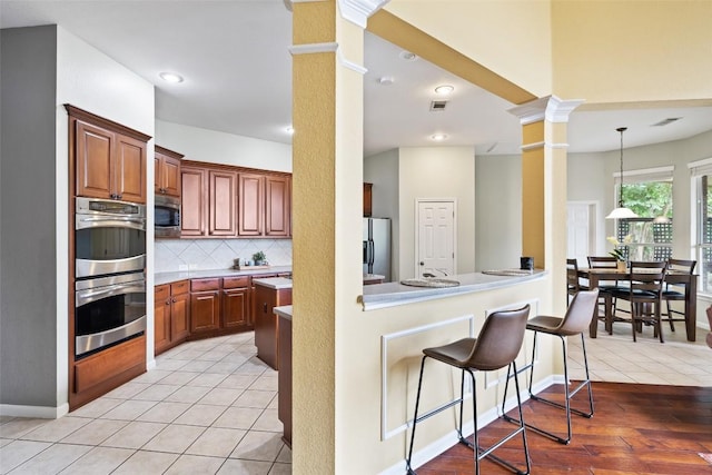 10129 Brimfield Dr, Austin, TX 78726 - kitchen featuring decorative columns, appliances with stainless steel finishes, a kitchen breakfast bar, tasteful backsplash, and light countertops
