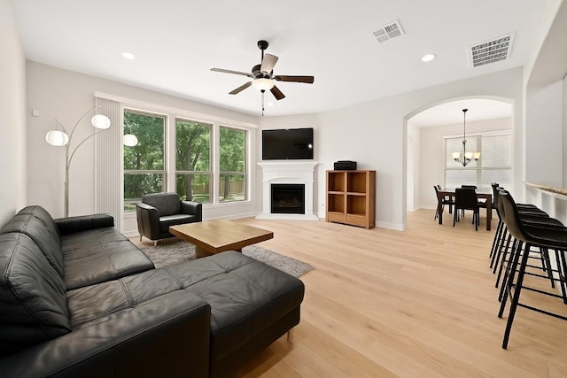 12404 Montclair Bnd, Austin, TX 78732 - living room featuring light wood-style floors, arched walkways, ceiling fan, a chandelier, and a fireplace with raised hearth