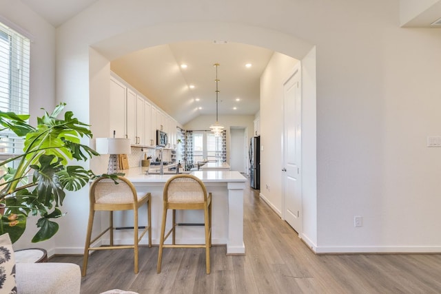 111 Blackwell Ln, Kyle, TX 78640 - kitchen with a peninsula, vaulted ceiling, light wood-style flooring, arched walkways, and white cabinets