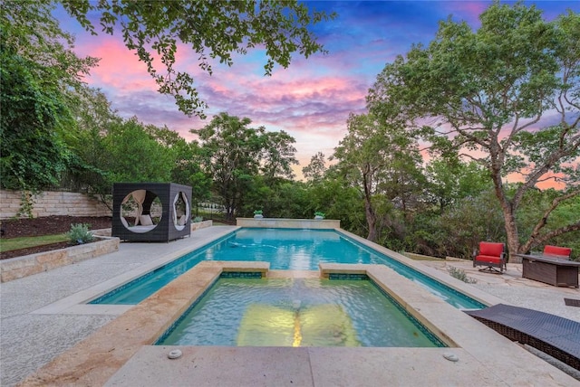 7116 Greenshores Dr, Austin, TX 78730 - pool at dusk featuring a patio, a pool with connected hot tub, and view of wooded area