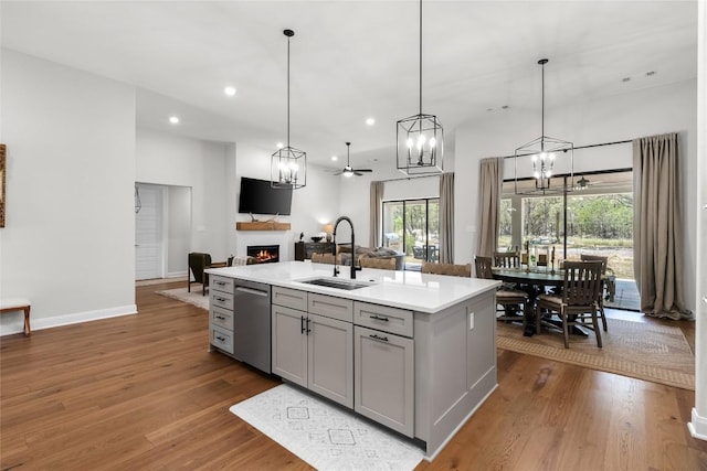 204 Love Creek Ct, Spicewood, TX 78669 - kitchen featuring gray cabinets, stainless steel dishwasher, a sink, a warm lit fireplace, and dark wood finished floors