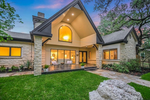 4715 Highland Ter, Austin, TX 78731 - back of house at dusk with stone siding, a lawn, a chimney, a shingled roof, and a patio