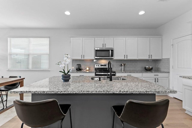 114 Ashford Way, Georgetown, TX 78626 - kitchen featuring appliances with stainless steel finishes, a sink, a kitchen breakfast bar, white cabinetry, and backsplash