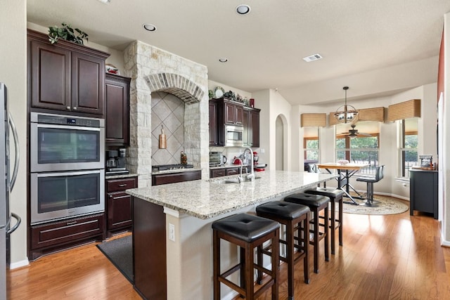 142 Abamillo Dr, Bastrop, TX 78602 - kitchen with appliances with stainless steel finishes, a sink, a kitchen island with sink, dark brown cabinets, and light wood-type flooring