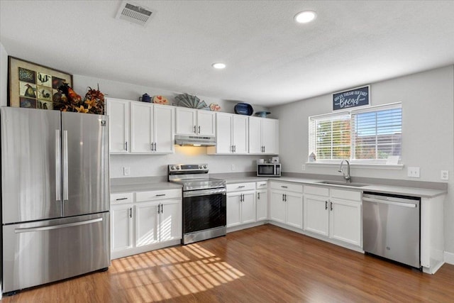 100 N Prairie Ln, Georgetown, TX 78633 - kitchen featuring appliances with stainless steel finishes, under cabinet range hood, white cabinetry, wood finished floors, and light countertops