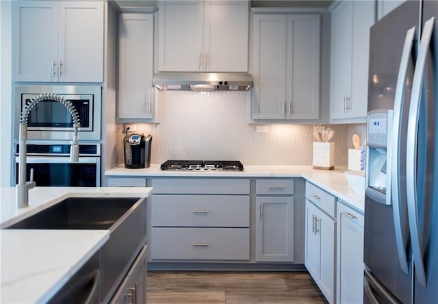 813 Vaughn St, Georgetown, TX 78628 - kitchen featuring stainless steel appliances, under cabinet range hood, gray cabinets, tasteful backsplash, and dark wood finished floors