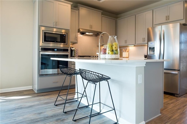 813 Vaughn St, Georgetown, TX 78628 - kitchen with appliances with stainless steel finishes, a kitchen island, under cabinet range hood, and light wood-style flooring