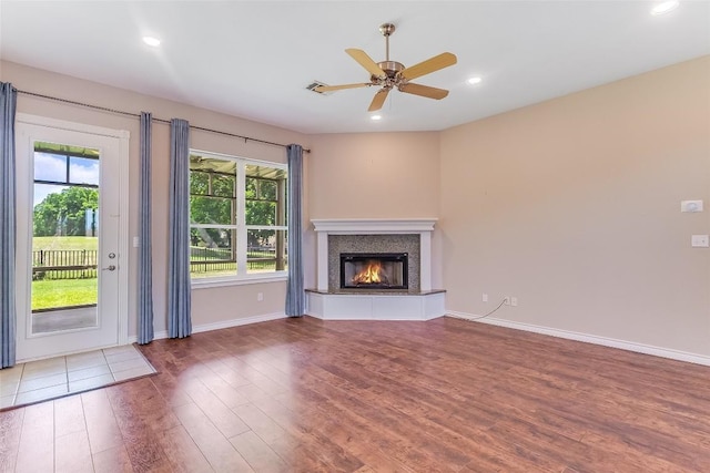 unfurnished living room with wood finished floors, a glass covered fireplace, ceiling fan, baseboards, and recessed lighting