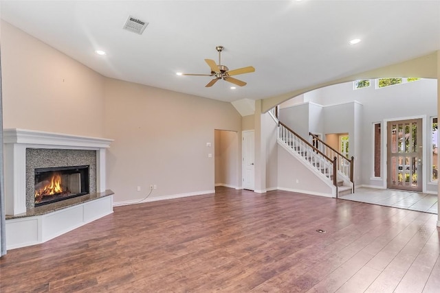 unfurnished living room with wood finished floors, stairs, a ceiling fan, vaulted ceiling, and a tile fireplace