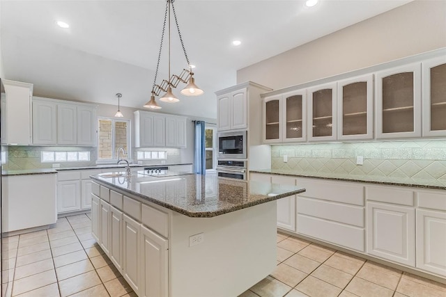 kitchen featuring oven, built in microwave, light tile patterned flooring, a center island with sink, and recessed lighting