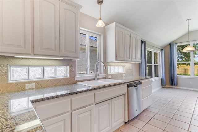kitchen featuring stainless steel dishwasher, a sink, vaulted ceiling, baseboards, and white cabinetry