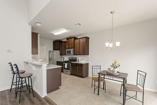 1701 S Bell Blvd Unit 101, Cedar Park, TX 78613 - kitchen featuring appliances with stainless steel finishes, dark brown cabinets, a breakfast bar area, tasteful backsplash, and a chandelier