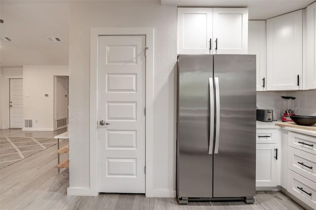 4601 Candletree Ln, Austin, TX 78744 - kitchen featuring freestanding refrigerator, white cabinetry, light countertops, light wood-type flooring, and tasteful backsplash