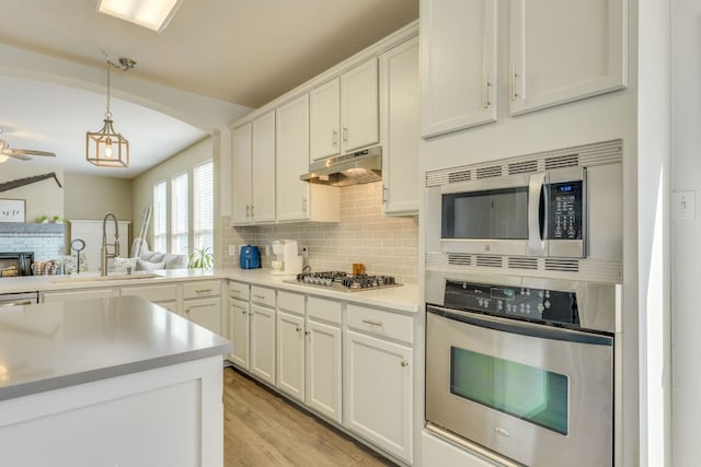 1414 Shamitas Ct, Leander, TX 78641 - kitchen featuring stainless steel appliances, under cabinet range hood, backsplash, hanging light fixtures, and white cabinetry