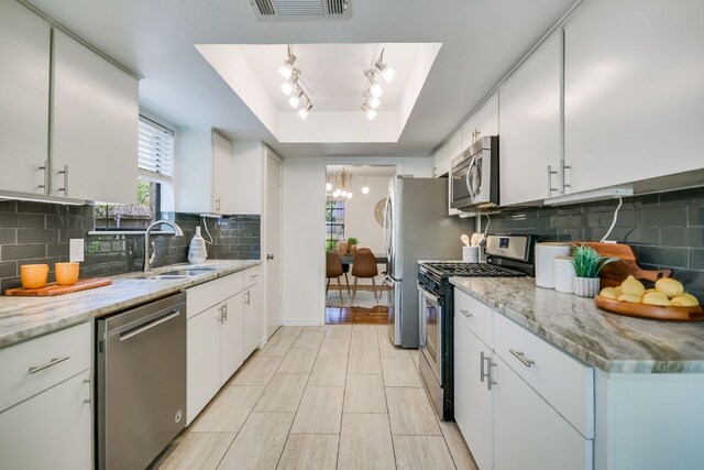 10300 Parkfield Dr, Austin, TX 78758 - kitchen featuring appliances with stainless steel finishes, a raised ceiling, a chandelier, white cabinetry, and decorative backsplash