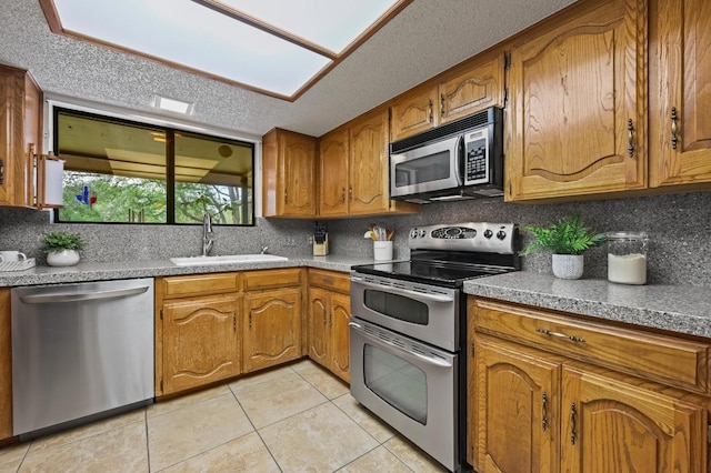 300 W Sequoia Spur, Georgetown, TX 78628 - kitchen featuring appliances with stainless steel finishes, a sink, light tile patterned flooring, brown cabinets, and a textured ceiling