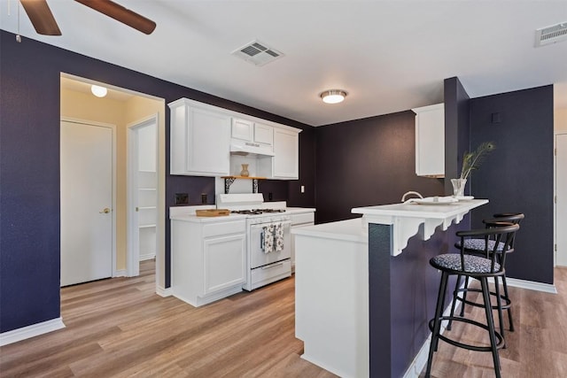 11607 Robert Wooding Dr, Austin, TX 78748 - kitchen with white gas range oven, a kitchen breakfast bar, light wood-type flooring, and white cabinetry