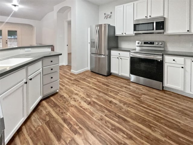 126 Waterlily Way, Hutto, TX 78634 - kitchen featuring appliances with stainless steel finishes, arched walkways, wood finished floors, dark countertops, and white cabinets