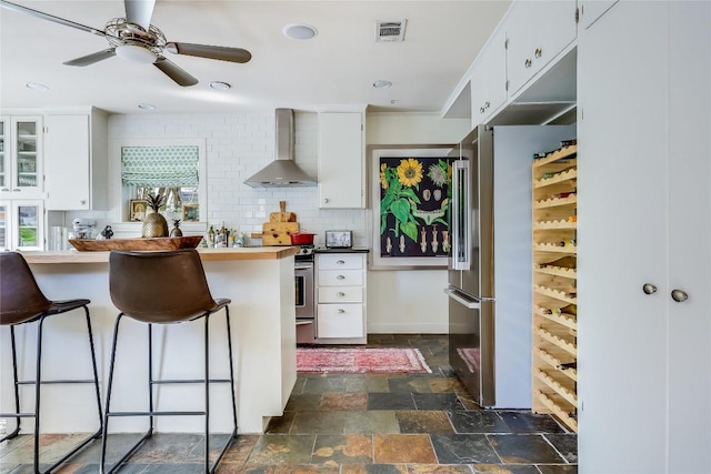 3202 Beverly Rd, Austin, TX 78703 - kitchen with wall chimney range hood, stainless steel appliances, stone tile flooring, white cabinets, and a breakfast bar area