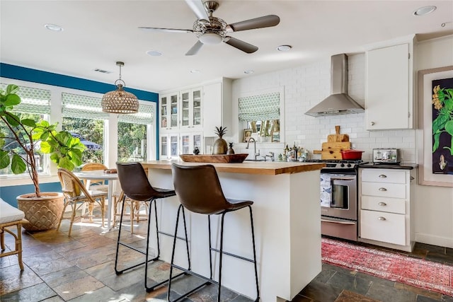 3202 Beverly Rd, Austin, TX 78703 - kitchen featuring wall chimney exhaust hood, stainless steel range oven, stone tile floors, white cabinets, and a kitchen breakfast bar