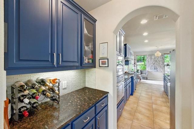 601 Harris Dr, Austin, TX 78737 - kitchen featuring blue cabinetry, stainless steel appliances, tasteful backsplash, arched walkways, and glass insert cabinets