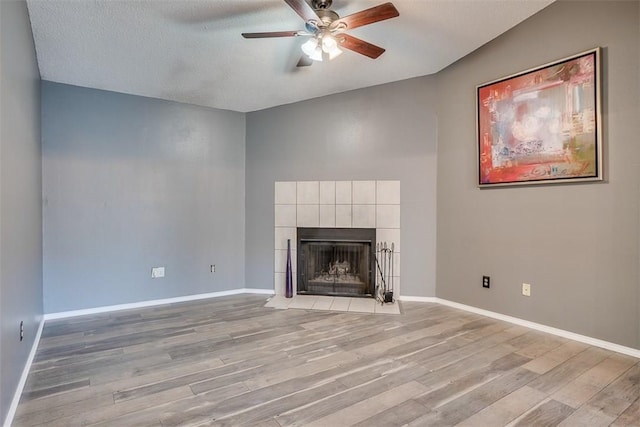 6009 Baton Rouge Dr, Austin, TX 78727 - unfurnished living room with ceiling fan, light wood-style flooring, a tile fireplace, baseboards, and a textured ceiling