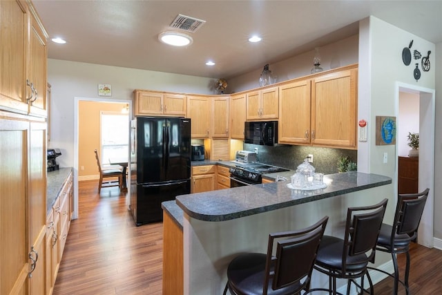 11525 Fm 86th Rd, Lockhart, TX 78644 - kitchen featuring black appliances, light brown cabinets, wood finished floors, a breakfast bar, and decorative backsplash