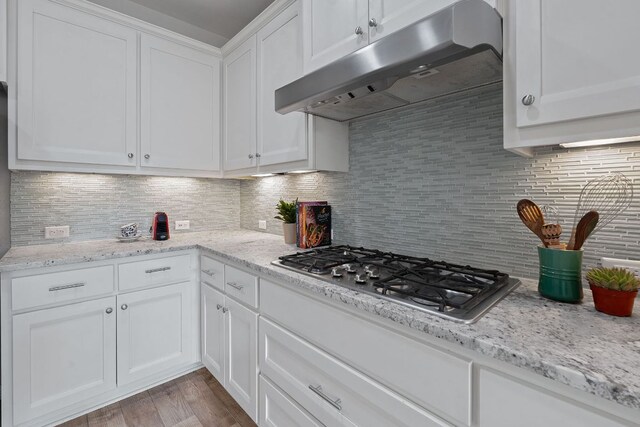 2809 Coral Valley Dr, Leander, TX 78641 - kitchen with under cabinet range hood, stainless steel gas stovetop, white cabinets, backsplash, and wood finished floors