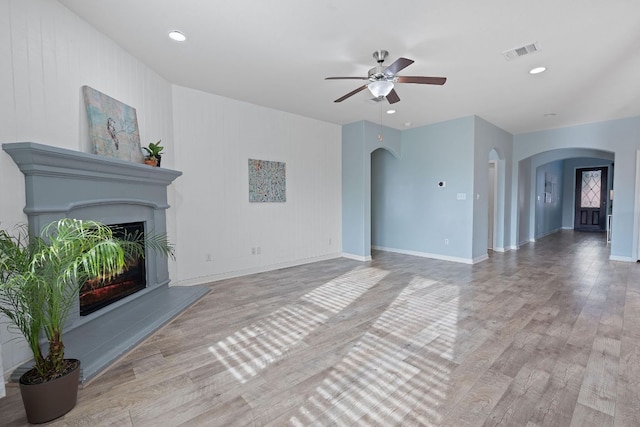 2809 Coral Valley Dr, Leander, TX 78641 - unfurnished living room with arched walkways, a ceiling fan, light wood finished floors, a glass covered fireplace, and recessed lighting
