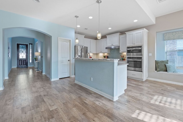 2809 Coral Valley Dr, Leander, TX 78641 - kitchen with under cabinet range hood, arched walkways, white cabinets, stainless steel appliances, and recessed lighting