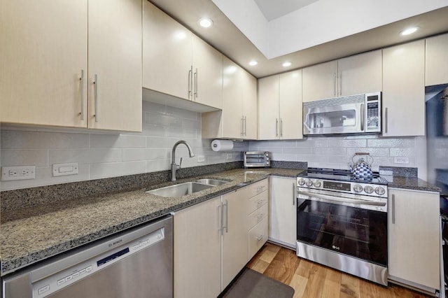 54 Rainey St Unit 814, Austin, TX 78701 - kitchen featuring stainless steel appliances, a sink, dark stone counters, light wood-style flooring, and tasteful backsplash