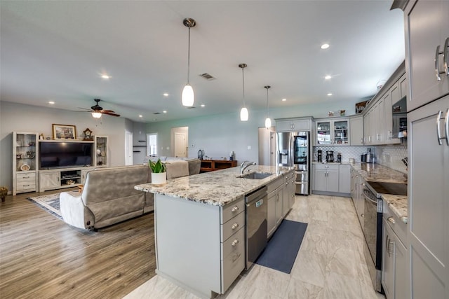 211 Spring Garden Dr, Hutto, TX 78634 - kitchen with gray cabinets, stainless steel appliances, a sink, a ceiling fan, and light stone counters