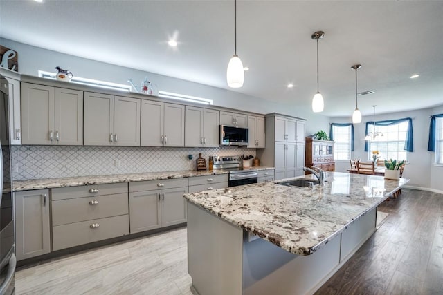 211 Spring Garden Dr, Hutto, TX 78634 - kitchen with gray cabinetry, stainless steel appliances, a sink, backsplash, and a kitchen island with sink