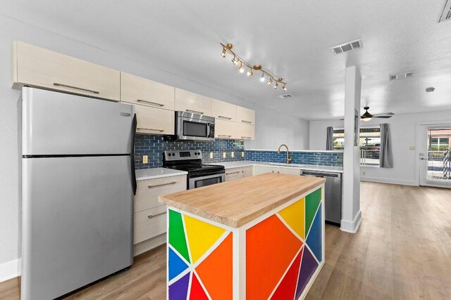 1101 Grove Blvd Unit 803, Austin, TX 78741 - kitchen featuring appliances with stainless steel finishes, decorative backsplash, light wood-style floors, ceiling fan, and a kitchen island