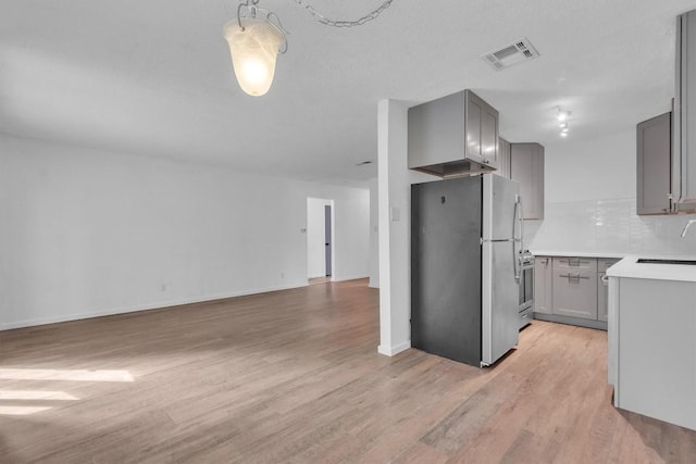 4406 Dove Springs Dr, Austin, TX 78744 - kitchen featuring freestanding refrigerator, gray cabinets, a sink, light wood finished floors, and backsplash