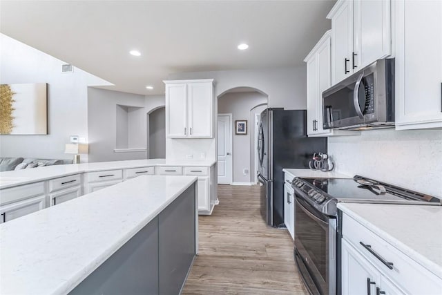 302 Emory Fields Dr, Hutto, TX 78634 - kitchen with electric range oven, stainless steel microwave, arched walkways, white cabinetry, and light wood-style floors
