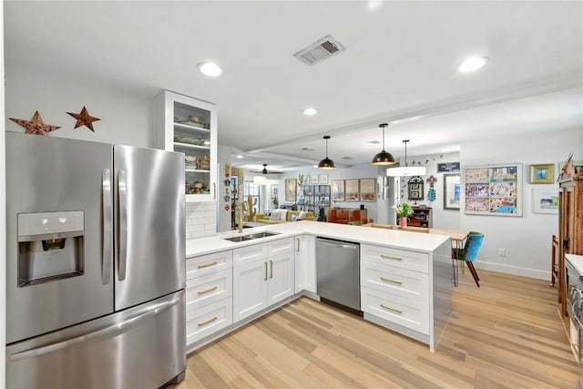 2406 Shiloh Dr, Austin, TX 78745 - kitchen featuring appliances with stainless steel finishes, a peninsula, light wood finished floors, white cabinets, and recessed lighting