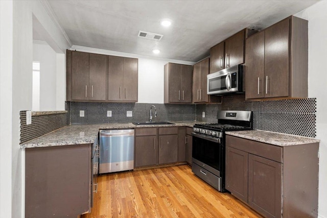 1307 Meadgreen Dr, Austin, TX 78758 - kitchen featuring appliances with stainless steel finishes, a sink, light wood-style floors, dark brown cabinets, and light stone countertops