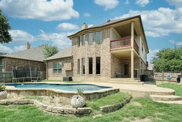 2937 Castellan Ln, Round Rock, TX 78665 - rear view of property with a balcony, a trampoline, brick siding, a chimney, and a fenced backyard