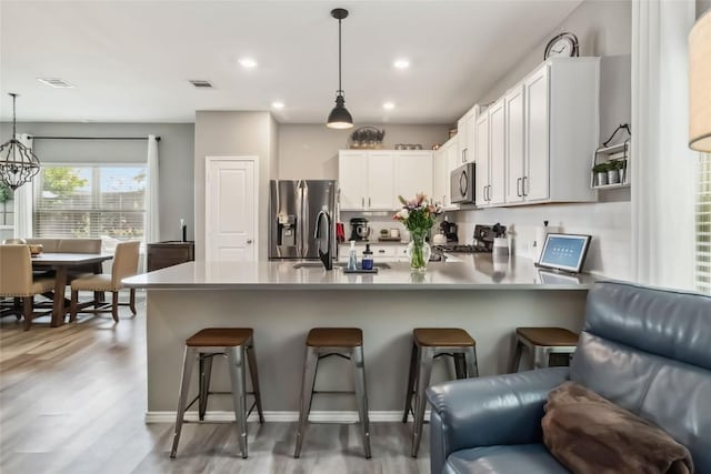 10901 Rome Ave, Austin, TX 78747 - kitchen with appliances with stainless steel finishes, a peninsula, a kitchen bar, hanging light fixtures, and light wood finished floors