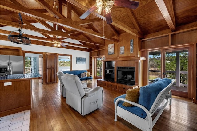 1514 Sunset Cliff Rd, Burnet, TX 78611 - living area featuring a ceiling fan, wooden ceiling with exposed beams, a tiled fireplace, light wood finished floors, and wooden walls