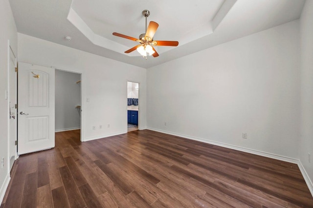 136 W Maple Dr, Granite Shoals, TX 78654 - unfurnished bedroom with a tray ceiling, a walk in closet, dark wood finished floors, baseboards, and connected bathroom