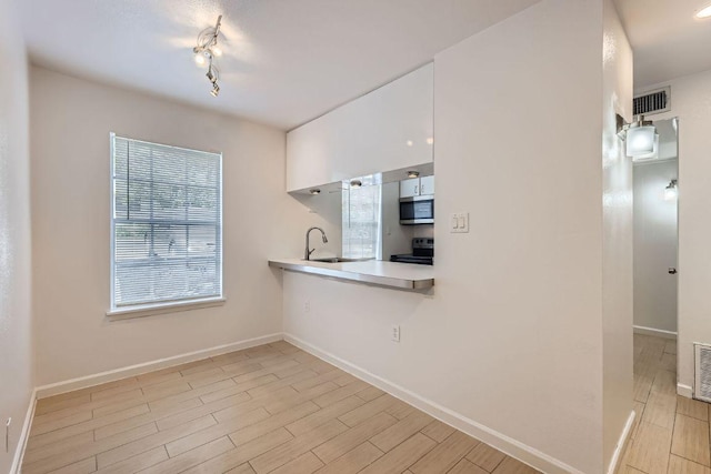 300 Crockett St Unit 115, Austin, TX 78704 - kitchen with stainless steel microwave, light countertops, a sink, white cabinets, and light wood-style flooring