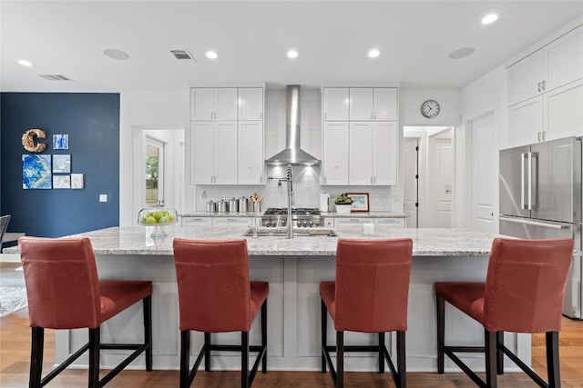 22005 Briarcliff Dr, Spicewood, TX 78669 - kitchen featuring wall chimney range hood, freestanding refrigerator, white cabinets, a large island with sink, and backsplash