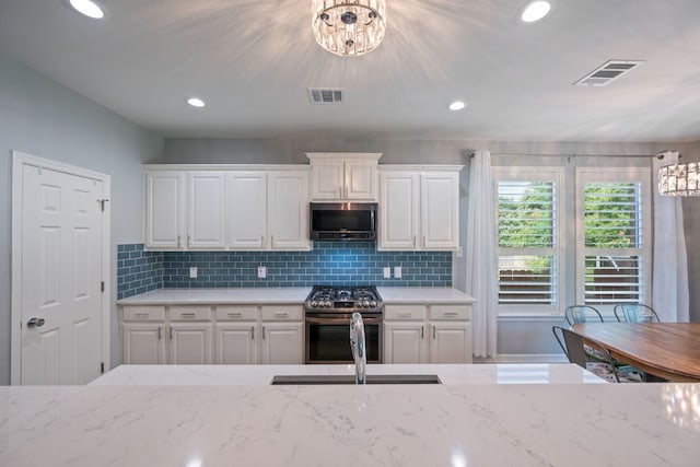19402 Gale Meadow Dr, Pflugerville, TX 78660 - kitchen featuring appliances with stainless steel finishes, white cabinetry, a chandelier, light stone counters, and decorative backsplash