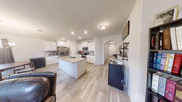 183 Beth Ann Loop, Taylor, TX 76574 - kitchen featuring appliances with stainless steel finishes, arched walkways, light wood-style flooring, white cabinetry, and a kitchen island with sink