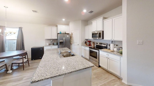 183 Beth Ann Loop, Taylor, TX 76574 - kitchen featuring stainless steel appliances, white cabinetry, a center island with sink, a chandelier, and light wood-style floors